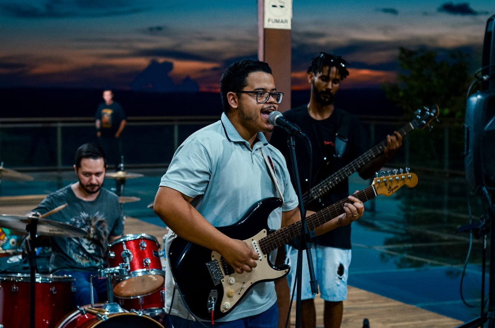 Geraldo Neto tocando guitarra e cantando ao microfone durante uma apresentação ao entardecer